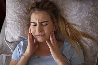 Jaw pain after waking up or sleeping, TMJ Bruxisum, teeth grindi young girl in bed in need of TMJ Treatment