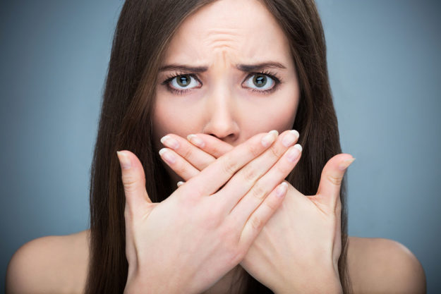 causes of bad breath woman covering her mouth as she is causing bad breath